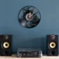 Wall clock with drum set design above a turntable and speakers on a blue wall background.