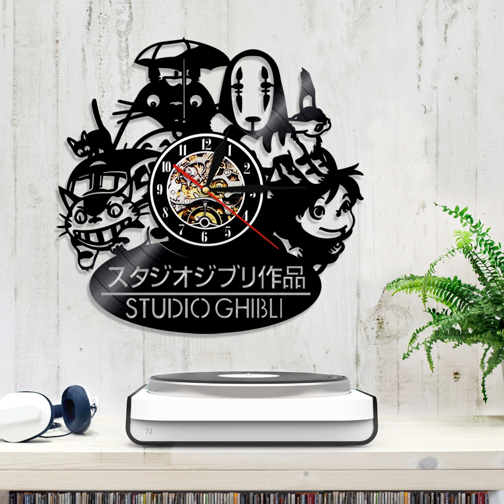 A Totoro Studio Ghibli Wall Clock with a modern design, showcasing various characters from Studio Ghibli, is mounted above a table that holds a speaker and headphones.
