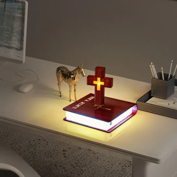 Christmas gift Personalized gifts home decoration Magnetic levitation cross floating crass table lamp RGB color 2 A desk with a decorative cross lamp on top of an illuminated book, next to a small giraffe figurine and a pen holder.