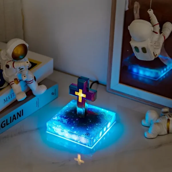 Christmas gift Personalized gifts home decoration Magnetic levitation cross floating crass table lamp RGB color 6 A glowing decorative cross on a blue illuminated base, surrounded by astronaut figurines and books on a table.