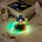 A glowing cross with a colorful light base is surrounded by small astronaut statues. Two books, including one by Matisse, are in the background on a fuzzy surface.