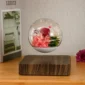 A glass orb with pink and red flowers floats above a wooden base on a table.