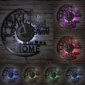 Wall clock with the phrase "The kitchen is the heart of the home" and cups design. Shown with different colored LED backlights on a brick wall.