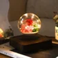 A levitating glass globe contains illuminated flowers and greenery, positioned on a wooden base on a table.