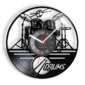 Vinyl record wall clock featuring a cut-out design of a drum set and the word "DRUMS" below. Clock hands are red and white with numbers on a circular face in the center.