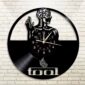 A round Skeletal Brain Wall Clock with a vinyl record design, featuring an artistic figure and the word "tool" engraved on it, mounted on a white brick wall.