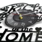 Close-up of a round vinyl-themed wall clock with white numbers and hands on a black face. The background features black decorative text and shapes.
