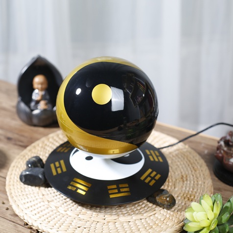 A Levitating Magic Ball in black and gold hovers above a device on a woven mat, surrounded by decorative stones and a small statue.