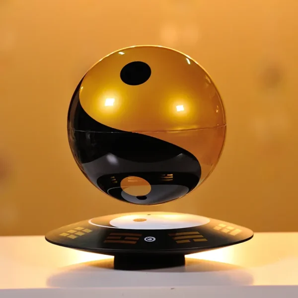 HCNT Feng Shui ornaments Yin and Yang Tai Chi ball home decoration levitation ball 2 A levitating speaker in the shape of a Yin and Yang symbol, with a reflective gold and black surface, floats above a matching base on a white surface.