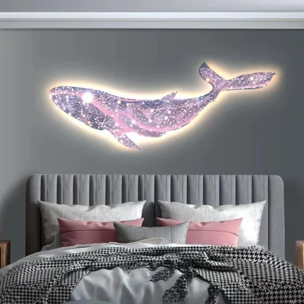 Modern luxury starry sky dream Whale living room sofa Background night light wall decoration bedroom atmosphere lightingPaintin 3 A glowing whale-shaped wall art with a galaxy pattern is mounted above a gray upholstered bed with pink and gray pillows and a houndstooth blanket.