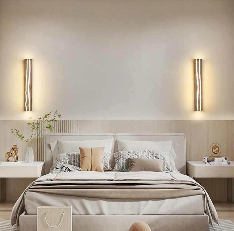 A modern bedroom with a beige color scheme, featuring a neatly made bed, two wall-mounted lights, and nightstands with decorative items.