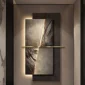 A modern wall art installation featuring two rectangular panels with textured, stone-like surfaces and a horizontal metallic bar across the center. The backlighting highlights the textures.