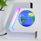 A small globe floats and rotates in mid-air within a C-shaped magnetic levitation frame, illuminated by colored LED lights, with a plant and white background visible.